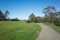 A concrete footpath/walkway in a large park with vast lawn areas