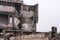 Concrete fragments of the destroyed foundation against the background of the remains of the building and the gray sky