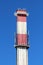 Concrete high red and white industrial chimney with two metal safety platforms and multiple cell phone transmitters