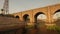 Concrete pathway alongside an urban canal going under an arched bridge. 3D illustration.