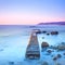 Concrete pier or jetty and rocks on a blue sea. Hills on background