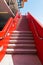 Concrete steps in a vibrant red stairway ascending along the exterior of a building into a perfect blue sky