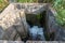 Concrete water permeable shaft close up, the dirty water from a small pond flowing out to a small creek