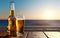 The condensation filled beer glass and the open beer bottle on the hardwood table. Light reflecting sea blurred into the