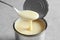 Condensed milk pouring from spoon into tin can on grey, closeup. Dairy product