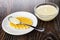 Condensed milk in spoon on cookie in saucer, bowl with condensed milk on wooden table