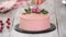 Confectioner decorates pink cake with roses.