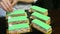 Confectioner hands decorate by white bizet six green glazed layered cake portions