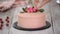 Confectioner pastry chef decorates creamy pink cake with fresh flowers on table