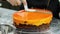 A confectioner pouring an orange topping over a cake