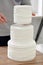 Confectioner stacking layers of white naked wedding torte cake