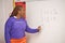 Confident African American female math teacher writing 
 numbers on the whiteboard in the classroom