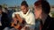 Confident African American guitarist playing in sunshine resting with multiethnic friends on rooftop. Side view portrait