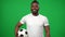 Confident African American man looking around and looking at camera standing at chromakey background with football ball