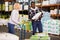 Confident African American warehouse worker with mature female assistant loading sacks with fertilizers on trolley cart