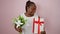 Confident african american woman overjoyed, smiling wide, holding birthday gift and lush bouquet, against pink isolated background