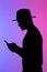 Confident african man silhouette using mobile phone while standing to neon background