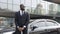 Confident Afro-American driver standing by car, security guard service, business