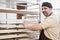 Confident baker posing with rack of fresh bread loaf at bakery.