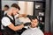 Confident barber shaving client`s beard with sharp razor.