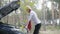 Confident blond woman coming to open car hood and looking at engine. Side view portrait of elegant blond Caucasian lady