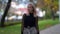 Confident blonde townswoman is strolling in park at early autumn day, looking at camera, medium portrait