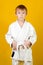 Confident boy in a white karate kimono over yellow background. Sports since childhood, discipline, first place, victory. Kids