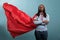 Confident and brave young superhero woman standing with arms crossed while wearing red mighty cape