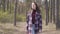 Confident brunette Caucasian woman walking in sunny forest. Portrait of happy young girl in plaid jacket strolling in