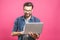 Confident business expert. Confident young handsome man in shirt holding laptop and smiling while standing against pink background