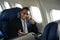 Confident businessman in black suit sitting comfortable seat in airplane cabin and talking on mobile phone