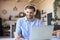 Confident businessman in earphones is writing notes or financial report while sitting at desk with laptop at home