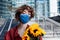 Confident businesswoman in facial mask is awaiting meeting, date, woman with bouquet of sunflowers is standing in financial centre