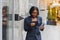 Confident businesswoman outside. Black woman in office suit standing near urban glass wall and using mobile phone. African