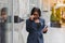 Confident businesswoman outside. Black woman in office suit standing near urban glass wall and using mobile phone. African