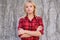 Confident calm woman with crossed arms, looking at camera. Beautiful young girl in checkered red shirt standing against grey backg