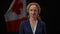 Confident Canadian female politician looking at camera smiling with national flag at black background. Portrait of