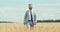 Confident caucasian businessman walking through wheat field and smiling, slow motion