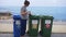 Confident Caucasian young woman taking off coronavirus face mask throwing garbage in Plastic waste bin on sea coast and