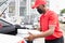 Confident deliveryman in red uniform puts orders in the car