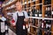 Confident elderly salesman of wine house arranging wine bottles on shelves rack
