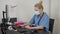 Confident experienced young doctor woman with face mask sitting in front of computer in office