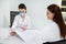 Confident female doctor in medical mask consults her patient, analyzes her medical records in a white office. Concept of a