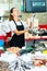 Confident female fishmonger working behind store counter, weighing fresh anchovies on scales