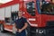 A confident firefighter strikes a pose in front of a modern firetruck, exuding pride, strength, and preparedness for