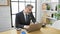 Confident grey-haired hispanic man engaged in a business talk over the phone, working online in office