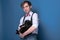 Confident handsome man in shirt, suspender and bow tie holding black cat and looking at camera