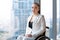 Confident happy businesswoman in wheelchair against the background of a panoramic window overlooking the skyscrapers and