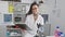 Confident hispanic amputee woman scientist, smiling and handling a clipboard in a bustling laboratory, pioneering research and