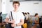 Confident interested teenage male student standing in technology classroom against background of rows of computers on